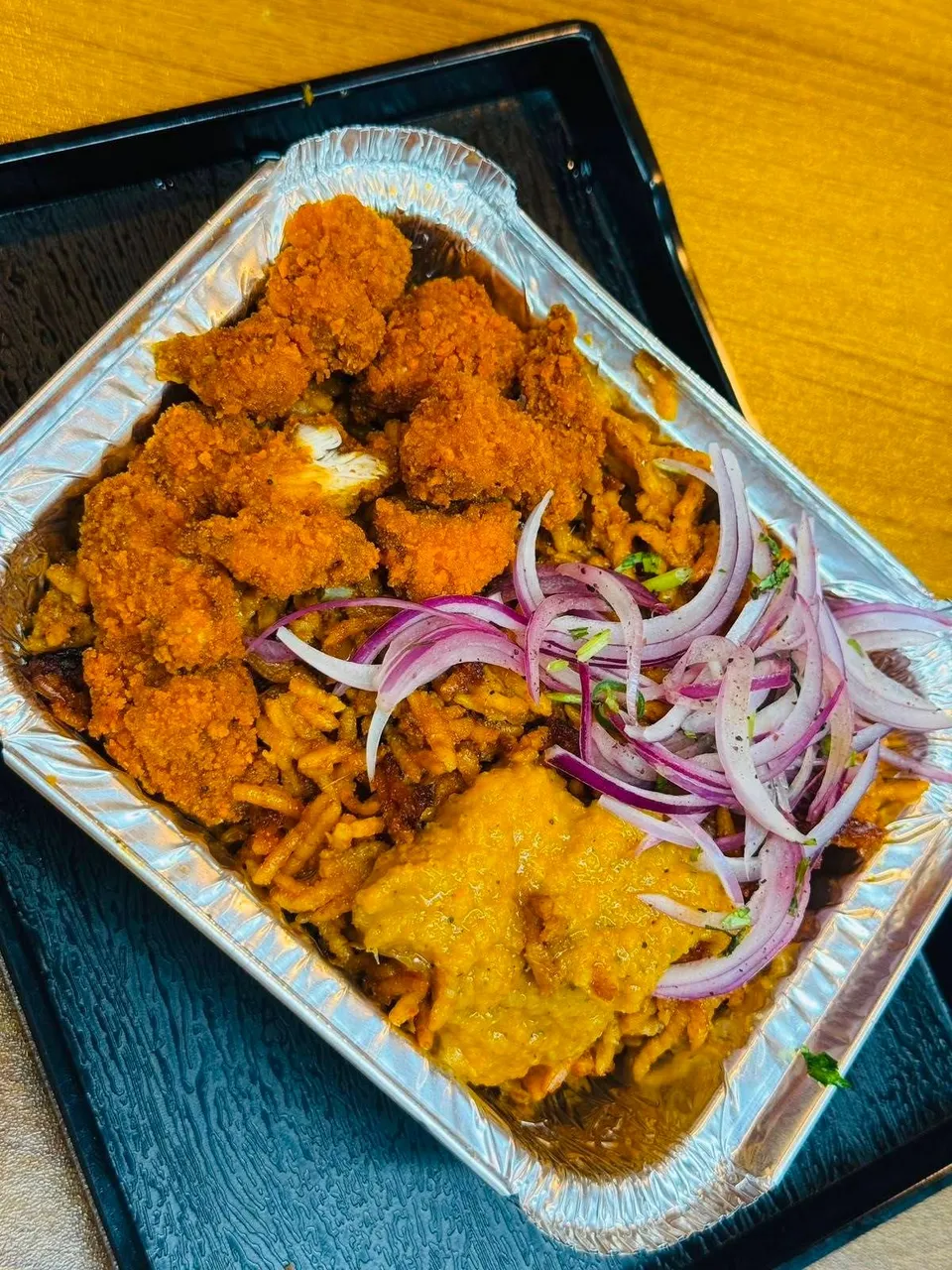 Crispy chicken over spiced rice in a takeaway tray
